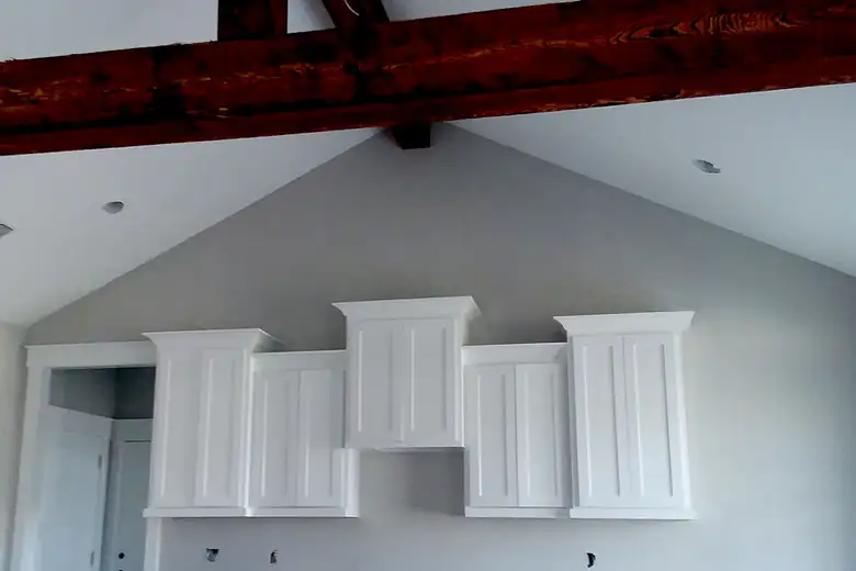 White floating upper cabinets on a grey wall under a timber beam