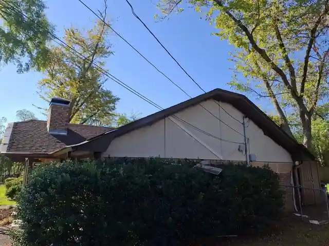 Side gable seen over a hedge with utility wires overhead
