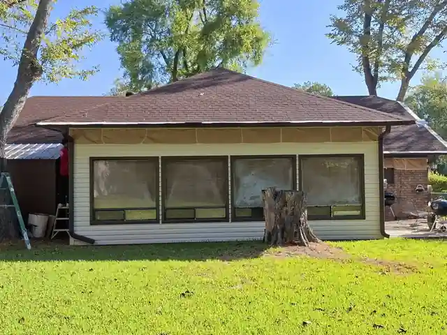Back sunroom windows masked in paper against cream siding, a stump in the yard