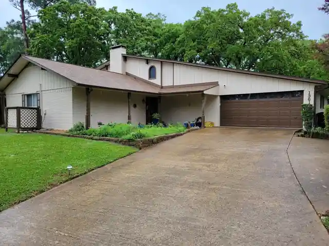 Cream-painted brick and siding home with a brown garage door, wet driveway and oaks