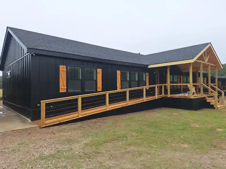 Black board-and-batten house with cedar shutters and a cedar ramp railing