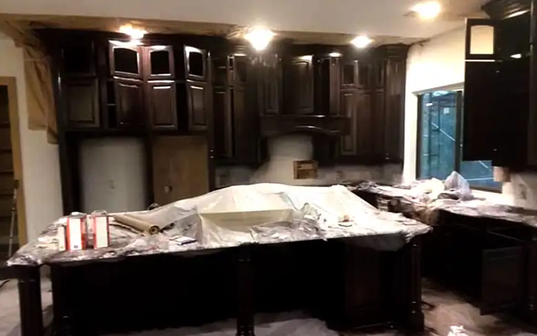 Kitchen cabinets freshly sprayed dark, the island still wrapped in clear plastic