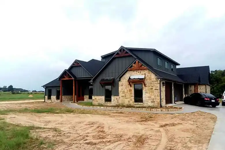 Stone and dark-siding ranch new build on a raw dirt yard