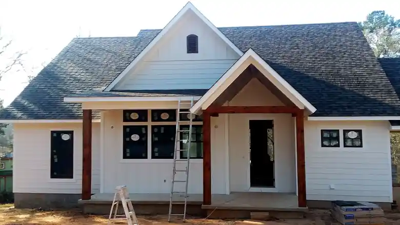 White board-and-batten new build with cedar porch posts and a ladder, mid-paint