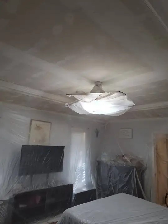 A tray ceiling with visible joint compound strokes, the ceiling fan bagged in plastic and the room tented