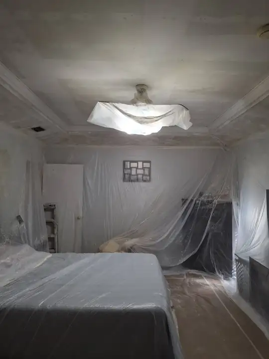 The bedroom during prep: bed and furniture sheeted in plastic, the ceiling fan bagged, the tray ceiling being skimmed