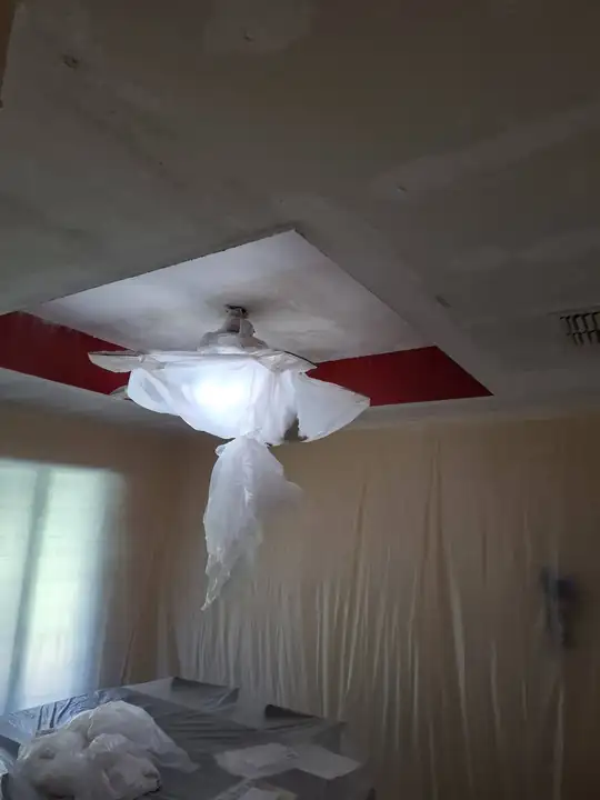 A patched tray ceiling with a red band, the fan wrapped in a plastic bag and the bed covered