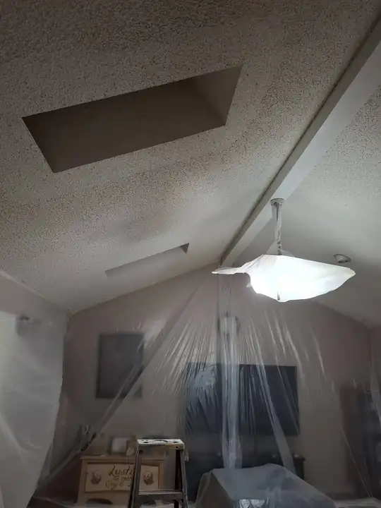 A vaulted living room sealed in clear plastic during prep, the light fixture bagged and glowing
